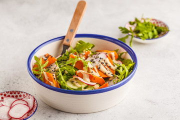 Bright vegan salad with arugula, sweet potato, radish, tahini dressing and cucumber, white background, copy space. Healthy vegan food concept.