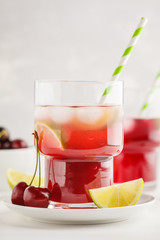 Cherry juice with ice and lime in a glass beaker, light background. White background.