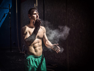 Shirtless man using chalk or magnesium powder in gym, clapping hands and creating cloud