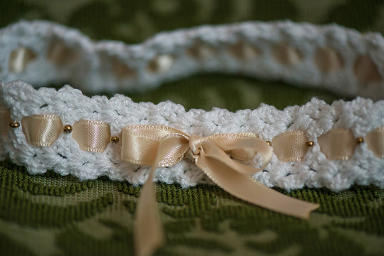 Cute baby girl head band in white with beige silk ribbon, cropped frontal view against an ornate cushion background, adorable accessory reserved for Christening or special events