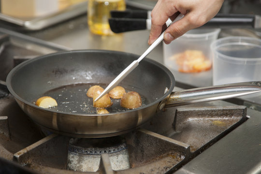 The hands of a cook preparing potatoes in a frying pan