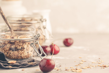 Homemade oat granola in glass jars with cherry and yogurt, copy space. Healthy food concept.