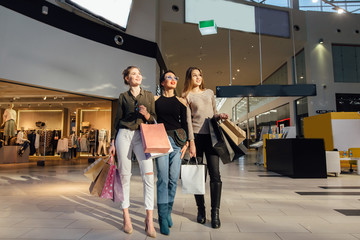 three glamorous girlfriends with shopping paperbags walking in mall