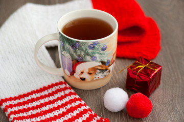 Tea in the New Year's mug. Image of a dog on a mug of tea, as a symbol of the year of the dog. Tea in the new year, red knitted scarf, Santa's cap create a New Year mood. New Year's dog.