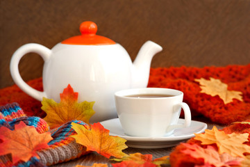 Autumn tea in orange tones. A teapot, a cup of tea and maple leaves surrounded by knitted orange shawls create coziness in the cold autumn season.