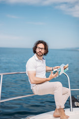 Obraz premium Young bearded man on a luxury yacht with a magnificent view of the sea. Sailing. Luxury yachts. Summer vacation and voyage concept.