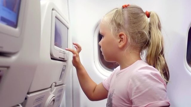Close up shot of a little blonde cutie playing with touchscreen in plane seat.