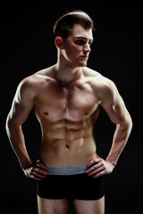 Handsome sporty young man in underwear posing on dark background