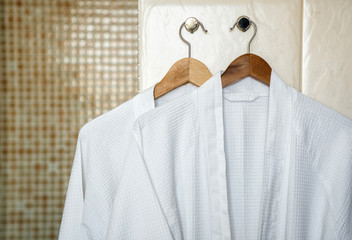 Two white rag bathrobes towels on wooden hangers in the interior of a stylish bathroom. Relax in...