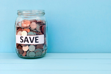 Money (coins) in the glass jar with the inscription "SAVE" on a turquoise background (concept, how to save money)
