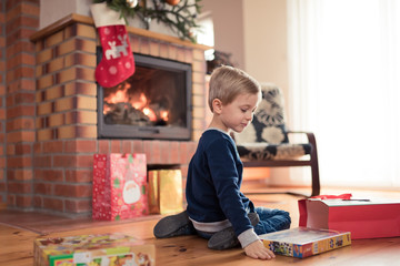 5 years old boy in front of the fireplace is happy with Christmas gifts.