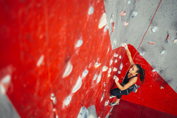 High angle view of sporty brown-haired woman exercising wall climbing on colorful red artificial...