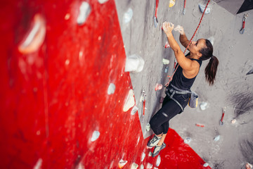 Young unrecognizable woman in black sportswear doing professional bouldering on grey and red rockat...