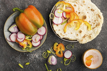 Traditional homemade flat breads for a snack with fresh seasonal vegetables, herbs and yoghurt sauce with olive oil and rose salt on the background. Top view