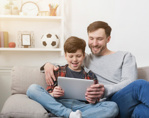Father and son using tablet together on sofa at home