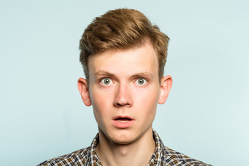 shocked speechless dumbstruck man with open mouth. portrait of a young guy on light background....
