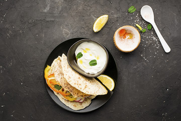 Traditional homemade flat breads for a snack with fresh seasonal vegetables, herbs and yoghurt sauce with olive oil and rose salt on the background. Top view