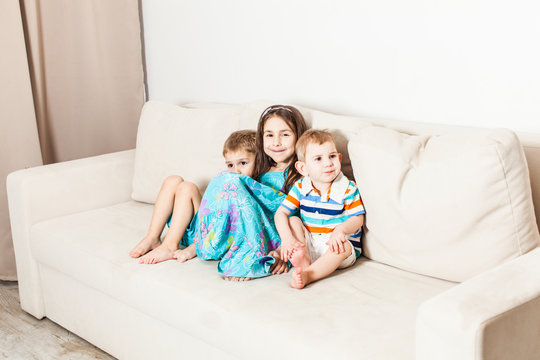 Three children are photographed sitting on the couch.