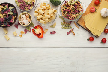 Assorted colorful pasta bowls on white wood, top view