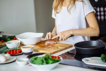 Cropped view of woman hands cutting meat on cutting board.
