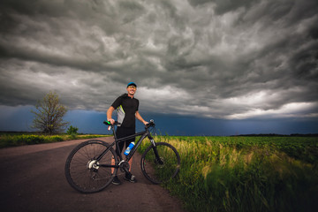 Happy man cyclist rides field road on a mountain bike. before the storm