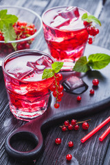 Red currant cocktail with ice and fresh mint on a black wooden table