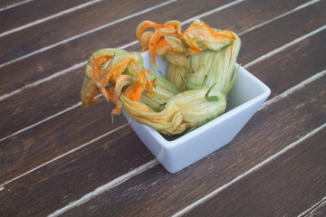 pumpkin flowers in white bowl on a wooden table seen close up