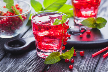 Red currant cocktail with ice and fresh mint on a black wooden table