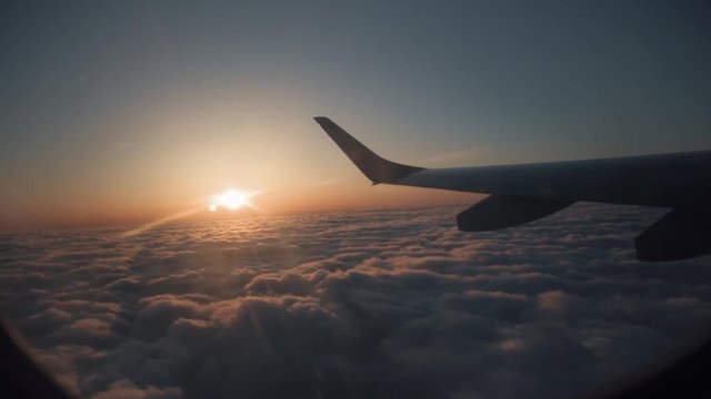 A view from the window seat of an airplane during sunset above the clouds.