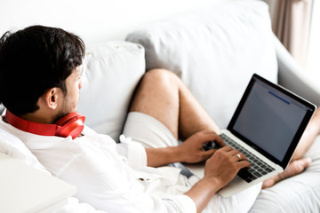 Happy man relaxing on the sofa listening to music with laptop at home