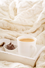 Obraz na płótnie Canvas Hot beverage mug with chocolate cookies in a white wool blanket. Hot drink, cozy home and cold season concept