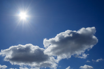 Fluffy clouds and midday sun in deep blue sky