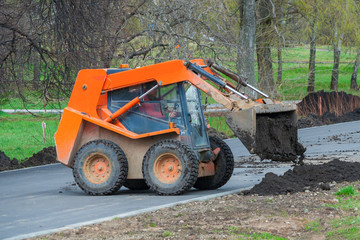 Small bulldozer unloads black soil. Works on the development of the park area. © Mikhail