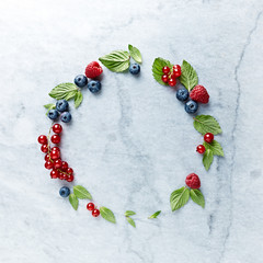 An Arrangement of fresh raspberries, blueberries, red currant and mint leaves on gray marble background. Flat lay. 