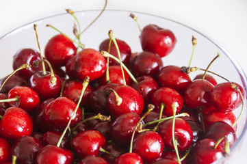 Obraz na płótnie Canvas Ripe cherries in glass bowl on white fabric background