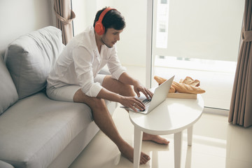 Happy man relaxing on the sofa listening to music with laptop at home