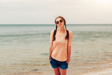 A hipster girl with braided hair in pigtails is walking along the beach in clothes. Summer concept, leisure tourism