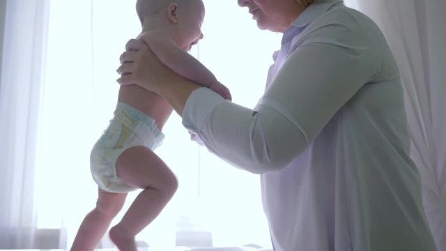 female physiotherapist makes exercise with infant baby and then takes it on hands in medical office