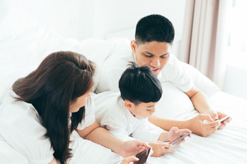 Asian boy playing smartphone with young parents lying in bed.Happy famility