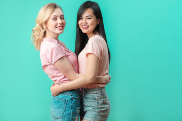 Two young multiracial women dressed in pink t-shirts and shorts, best friends standing face to face, embracing, looking at camera with happy expression