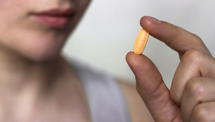 Girl holds an orange capsule in her hand, close-up, isolated on a neutral gray background. medical concept. Selective focus.