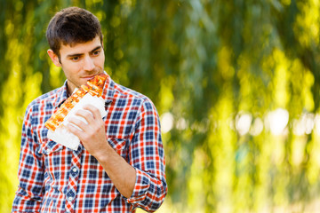 Naklejka na ściany i meble Cheerful young guy is eating pizza on the park