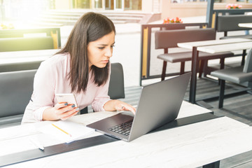 Focused young woman working in office, sitting at desk, using laptop, holding the phone