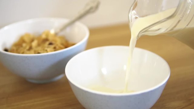Fresh and healthy caw milk slowly pouring in the white bawl. Healthy food and flakes at the background. Serving breakfast from quality products ( flakes and oat ) as the healthy meal for morning.