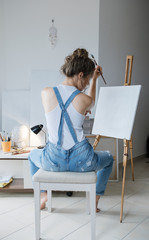 In search of inspiration. Sad Woman painter in front of the canvas and drawing. Artist studio interior. Process in art workshop.