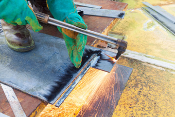 Industrial welder worker holding welding torch during perform welding sheet metal steel plate in construction factory by wearing heat protection gloves with smoke, spark, arc, fire, flash, hot