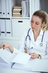 Bureaucracy in the hospital. Young female doctor work with stacks of files. - 211502648