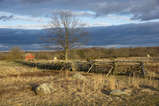 A wooden split rail fence and red barn stand lonely in a field in Gettysburg National Battlefield in Gettysburg, Pennsylvania, home to one of the bloodiest battles in the American Civil War. 