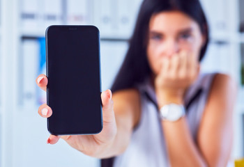 Young sad woman showing a blank smartphone screen. Focus on smartphone. Free space for your message.