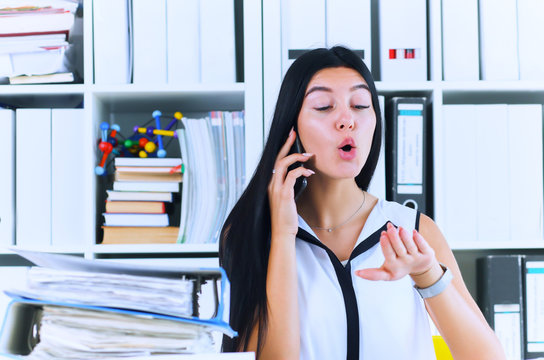 Young Secretary Talking On The Phone Forgets About A Lot Of Paper Work, Which Is Not Done. Inefficient Use Of Working Time